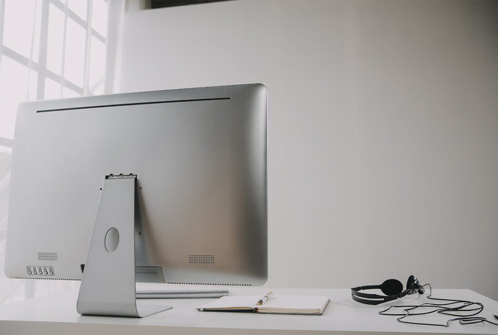 Ordenador de sobremesa en una mesa con unos cascos y una libreta de apuntes